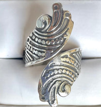 macro view of an intricate sterling silver bypass wrap ring featuring antiqued scrollwork, dot embossing, and an ornate filigree shield pattern