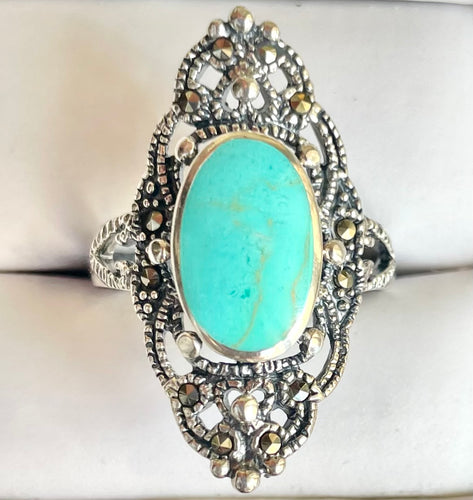 Front view of an elongated 925 sterling silver statement ring featuring a large oval turquoise cabochon center stone inside an ornate marcasite-accented filigree frame