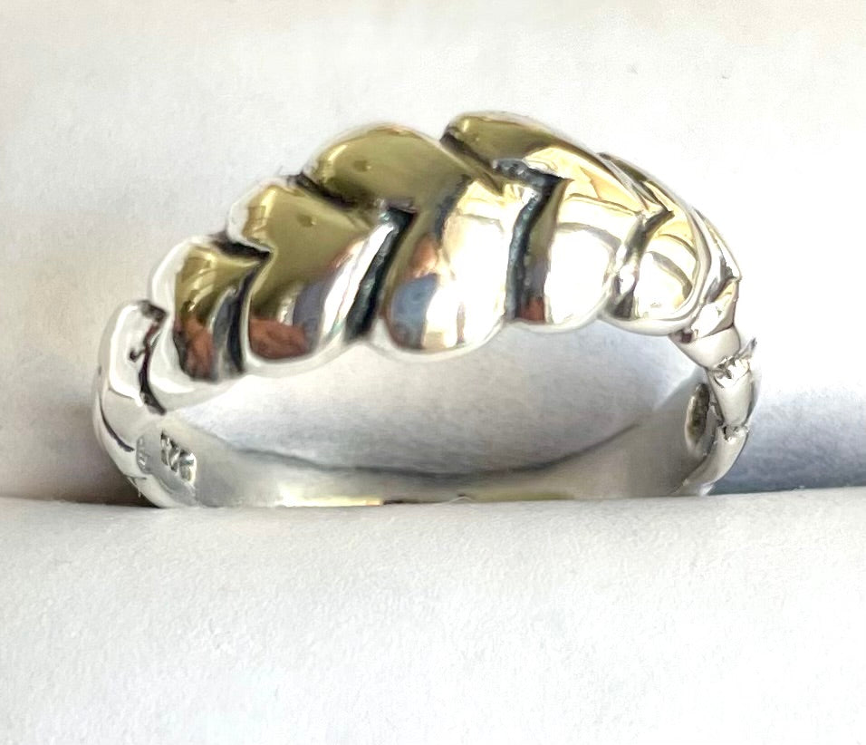 Close-up of a chunky sterling silver statement ring featuring a bold, interlocking herringbone braid design and high-polish finish.